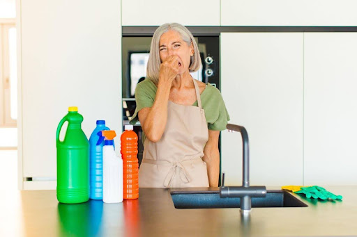 Older woman standing in front of kitchen sink holding nose from bad smalling wafting from sink drain.