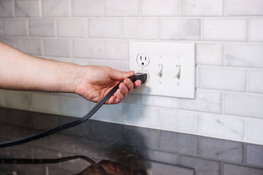 A hand plugging a device into an outlet on a kitchen countertop.