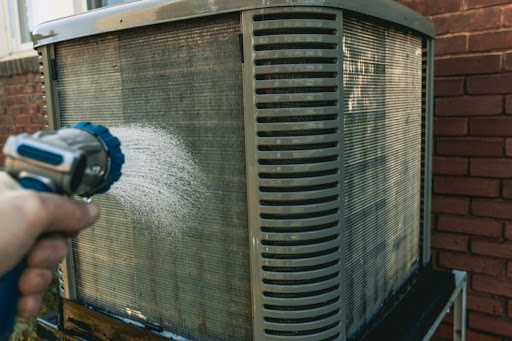Someone using a hose to spray down an outdoor AC unit.
