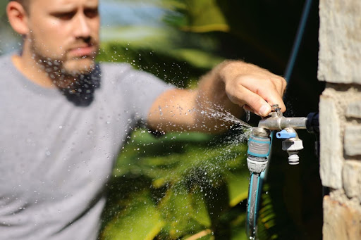 A man turning a handle on an outdoor faucet that's leaking water.