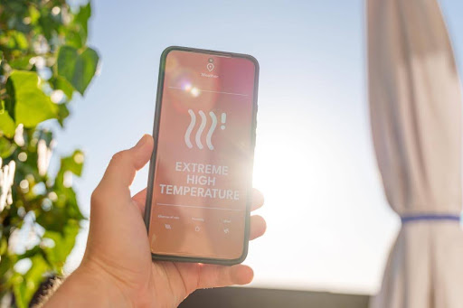 A person holding up a phone that reads "extreme high temperature" on the screen.